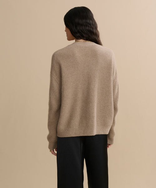 A person with long, dark wavy hair is seen from behind in the Cropped Cashmere Cocoon Cardigan and black pants, standing against a plain beige background.