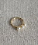 The Elodie Pearl Ring is a 14k gold fine jewelry piece featuring three luminous white pearls, displayed elegantly on textured beige fabric.