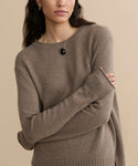 A person with long dark hair stands with arms crossed against a beige background, wearing the Everyday Sweater and a black pendant necklace.