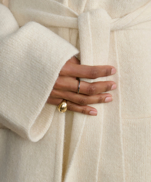 A close-up of a hand wearing the Felix Dome Ring in 14k solid gold and a thin silver band, resting on the waist of a person dressed in a soft, cream-colored belted coat from Jenni Kayne Jewelry.