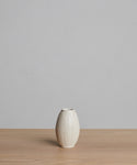 The Porta Ceramic Vase, small and cream-colored with vertical ridges, sits on a light wooden surface against a plain light gray background.