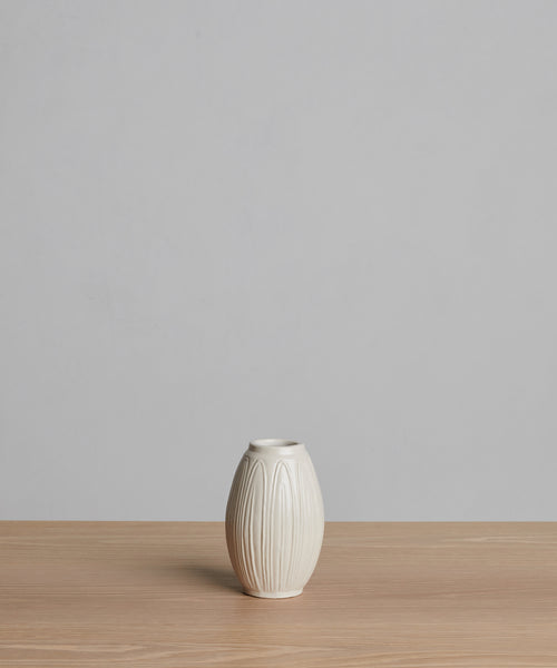 The Porta Ceramic Vase, small and cream-colored with vertical ridges, sits on a light wooden surface against a plain light gray background.