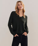 A person with long blonde hair wears the Flynn Cashmere Sweater in a relaxed fit with black jeans, standing hands in pockets against a plain light background.