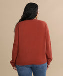A person with long dark hair is shown from the back, wearing the Flynn Cashmere Sweater in a relaxed rust color and blue jeans, standing against a plain beige background.