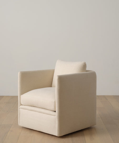 The Dume Chair is a modern accent piece with cream-colored hemp plush upholstery, clean lines, and a boxy shape. It features cushioned seat and back, set on a light wood floor against a plain, light wall.