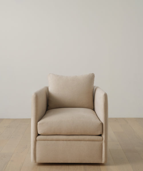 The Dume Chair, a beige hemp-upholstered accent seat with plush cushions, sits on a light wooden floor against an off-white wall, offering sustainable and stylish furniture.