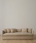 The Dume Sofa, a minimalist beige hemp piece handmade in Los Angeles with sustainable upholstery, includes four matching cushions and sits against an off-white wall on a light wooden floor.
