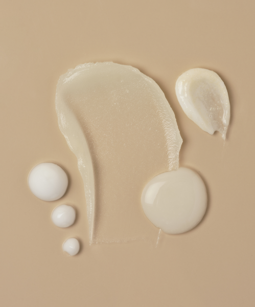 A smooth beige background displays textures from The Youthful Skin Routine: a large translucent smear, a creamy white dollop, three small white droplets, and an off-white swirl—highlighting its deep hydration and anti-aging benefits.