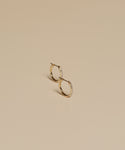 A pair of Iris Diamond Hoops in 14k gold, adorned with subtle diamonds, displayed on a smooth beige surface.