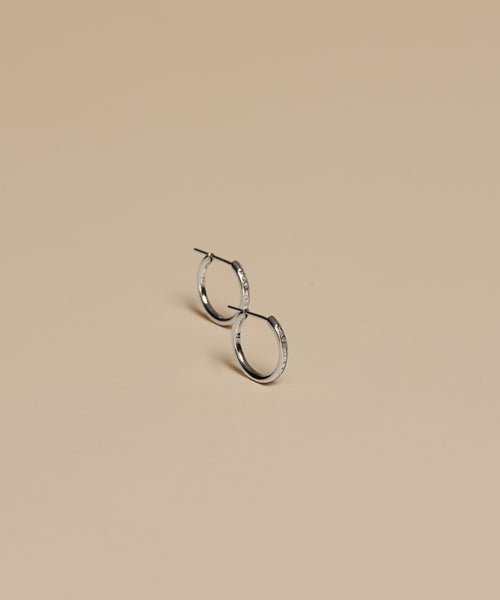 The Iris Diamond Hoops are small silver earrings with a smooth finish, shown upright on a beige background—ideal for layering with your favorite Jenni Kayne pieces.