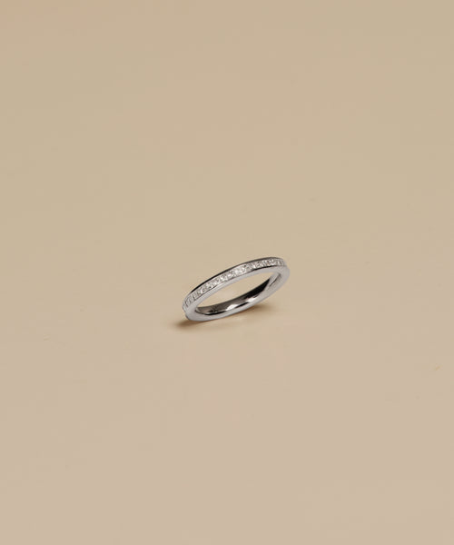 The Iris Eternity Band, crafted in white gold and adorned with a continuous row of sparkling diamonds, is elegantly presented on a simple beige background.