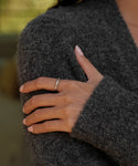 A hand with neatly manicured nails rests on a fuzzy dark gray sweater, showcasing the elegant June Baguette Band on the ring finger.