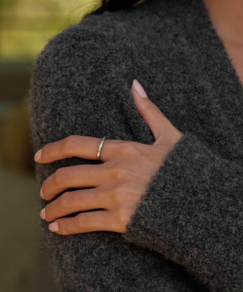 A hand with neatly manicured nails rests on a fuzzy dark gray sweater, showcasing the elegant June Baguette Band on the ring finger.