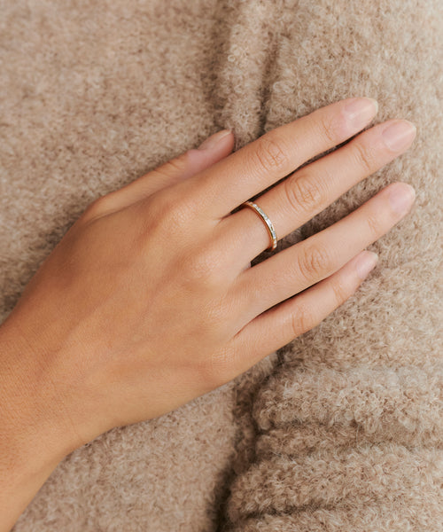 A hand wearing the June Baguette Band in 14k gold rests on soft beige fabric, with neatly trimmed natural nails, highlighting the understated elegance of Jenni Kayne jewelry.
