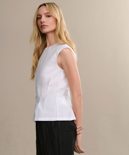 A woman with long blonde hair wears the Lara Top and black pants, standing sideways against a neutral beige background and looking confidently at the camera.