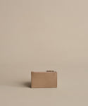 The Leather Card Holder, in taupe with a zippered closure, is centered on a beige background for a minimalist, monochromatic look—ideal for anyone who prefers to travel light.