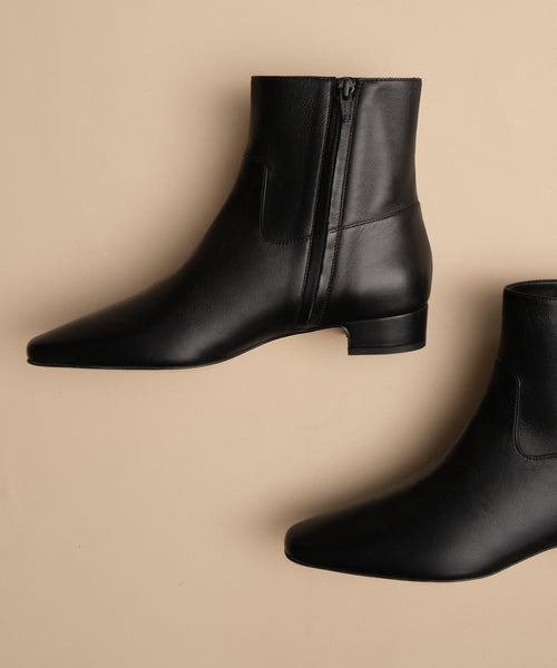 The Leather Carmine Boot is a sleek pair of black leather booties with low heels, offering both comfort and timeless style.