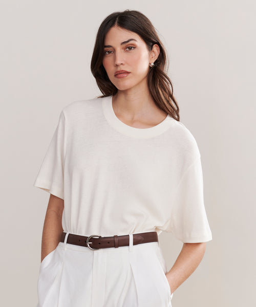 A woman with long brown hair wears a white short-sleeve tee, white high-waisted pants, and the Classic Belt, standing against a plain light background and looking at the camera with a neutral expression.