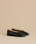 The Leather Elodie Flat, a pair of sleek black Italian-made flats with rounded toes and a feminine silhouette, is displayed on a light beige background.