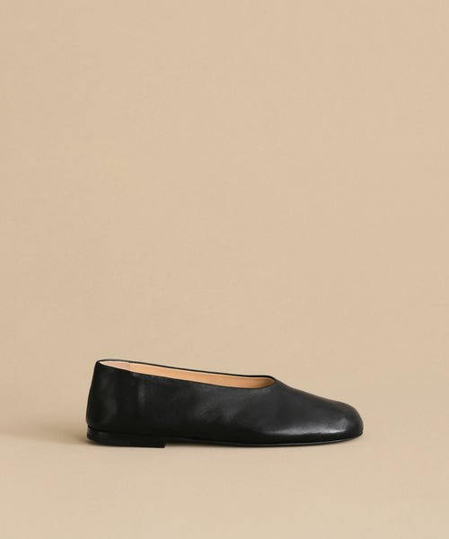 The Leather Elodie Flat, an Italian-made shoe with a rounded toe and low heel, is displayed against a plain beige background to showcase its classic feminine silhouette.