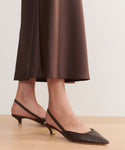 Wearing a brown satin midi skirt and Leather Kitten Heel shoes, made in Italy, a person stands on a light wooden floor. The photo focuses on their lower legs and feet.