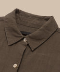 A close-up of the Linen Logan Shirt highlights its boxy fit, pointed collar, and light buttons, showcasing effortless style against a beige background.