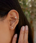 A close-up shows a woman wearing Small Loren Pearl Studs in her lobe and a 14k gold ear cuff with two pearls. Her manicured hand rests near her ear, highlighting the elegant design of Jenni Kayne Jewelry.