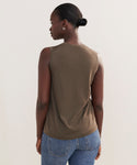 A woman with dark skin and hair in a low bun models the Merino Tank, paired with blue jeans, as she stands with her back to the camera against a plain light background.