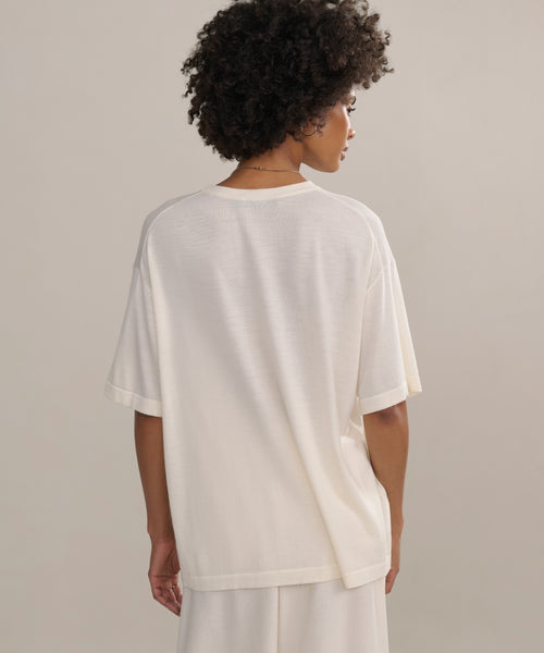 Person with short curly hair wears an oversized Merino Tee in white with matching white pants—an elevated basic, shown from the back against a neutral background.