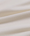 Close-up of soft, ivory-colored fabric from the Merino Tee. Gentle folds and a smooth, finely woven surface showcase the tee’s elevated basic style and subtle shadows.