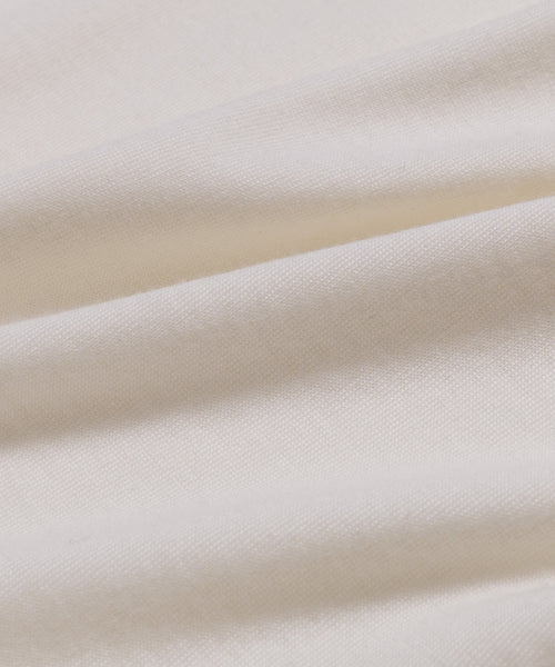 Close-up of soft, ivory-colored fabric from the Merino Tee. Gentle folds and a smooth, finely woven surface showcase the tee’s elevated basic style and subtle shadows.