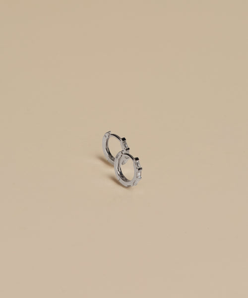 The Merit Baguette Hoops are small 14k white gold hoop earrings shown on a plain beige background, making them ideal as timeless heirloom jewelry.