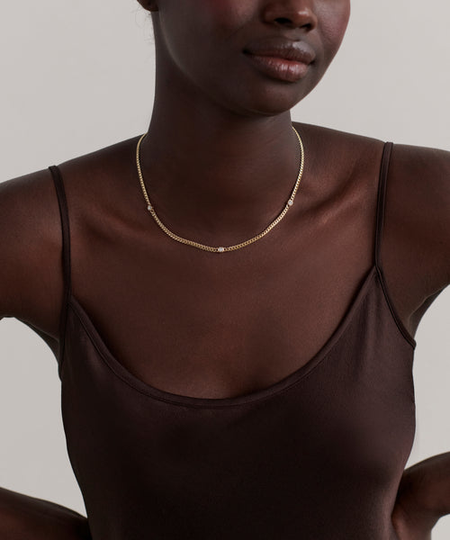 A woman wears a dark brown spaghetti strap top and the Merit Round Cut Diamond Necklace, posed against a plain light background.