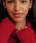 A woman with long dark hair, wearing a red knit sweater and the Mermaid Earrings, smiles softly at the camera while holding up her sweater’s collar.