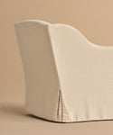 A close-up side view of the Miramar Chair, upholstered in light beige Belgian linen with a fitted slipcover, shown against a matching beige background.
