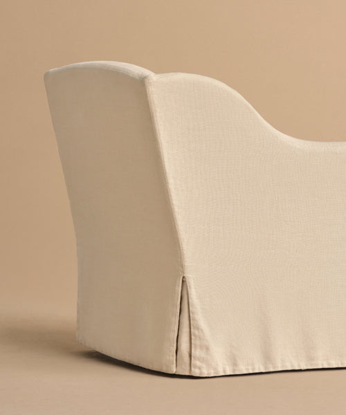 A close-up side view of the Miramar Chair, upholstered in light beige Belgian linen with a fitted slipcover, shown against a matching beige background.