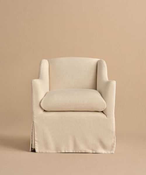 The Miramar Chair features a cream-colored linen slipcover, skirted base, plush seat cushion, and gently curved arms. Its modern, minimalist design stands out against a matching beige background.