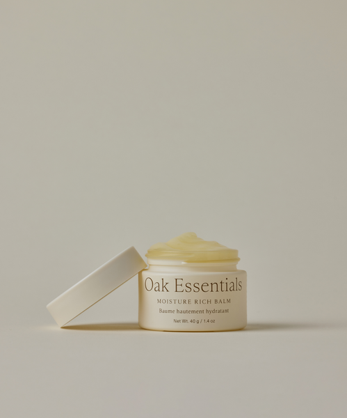 A jar of Moisture Rich Balm with its lid off reveals the creamy formula inside. The off-white container sits on a neutral background and deeply nourishes skin for a radiant, moisturized complexion.