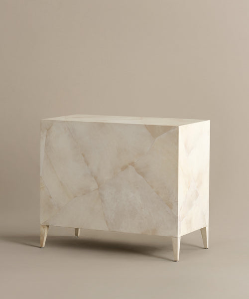 The Napa Dresser is a rectangular, off-white dresser with geometric angular patterns, tapered legs, and solid maple drawers, shown against a plain beige background.