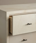 A close-up of the Napa Dresser shows a partially open solid maple drawer with a small black bow-shaped handle and soft-close glides. The dressers beige surface has a smooth, stone-like finish.