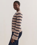 Wearing the Cooper Cardigan in taupe/navy stripes, featuring a structured silhouette, and dark jeans, a person stands sideways and smiles gently against a plain light background.