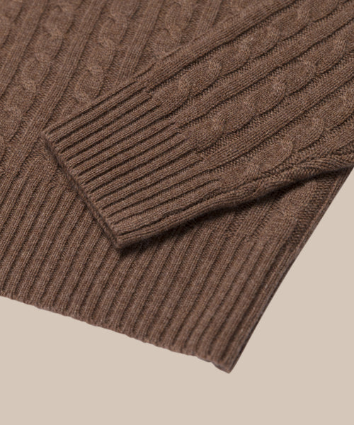 Close-up of the Nell V-Neck Sweater in brown, highlighting its cable knit texture and ribbed sleeve and hem cuffs against a beige background—ideal for fans of relaxed fit sweaters.