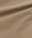 A close-up of smooth, light brown khaki fabric with gentle folds and soft shadows highlights the texture and subtle creases of the Italian cotton poplin featured in our Newport Trouser.