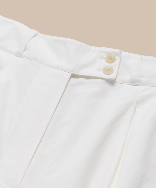 Close-up of the waistband and upper section of the Newport Trouser in white cotton poplin, with two beige buttons and pleated details, shown against a light beige background.
