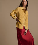 A woman with long dark hair poses against a beige background, wearing the Nina Slip Skirt in crimson and a mustard yellow jacket, looking slightly to the side with a neutral expression.