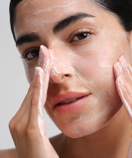 A person gently applies Nourishing Cleansing Milk to their face with both hands, highlighting smooth skin and natural features—ideal for sensitive skin.