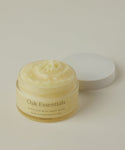 A glass jar of Moisture Rich Body Balm with a white lid sits on a light beige background, revealing its creamy, whipped texture enriched with cocoa butter inside.