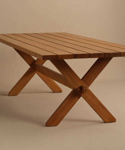 The Outdoor Garden Dining Table features a teak slatted top and crossed X-shaped legs, shown against a plain beige background.