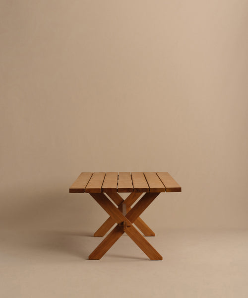 The Outdoor Garden Dining Table features a slatted rectangular teak top and crossed legs, shown against a plain beige background.