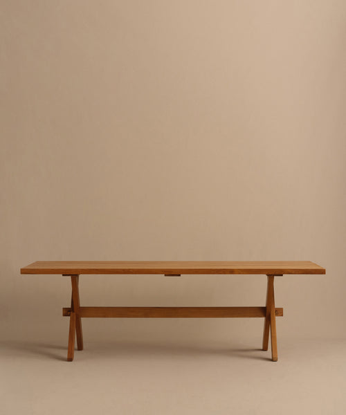 The Outdoor Garden Dining Table features a long, minimalist teak design with a rectangular top and simple trestle legs, shown against a plain beige background.